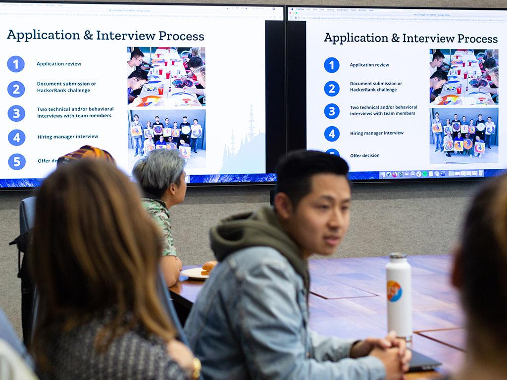 Students at a table look at career slides on large monitors