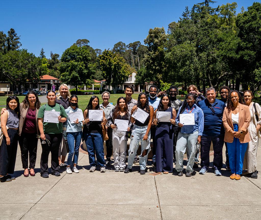 Students and staff stand with certificates in front of the fountain behind Mills Hall on the Oakland campus.