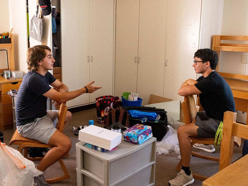 Two students sit on chairs and talk in dorm room