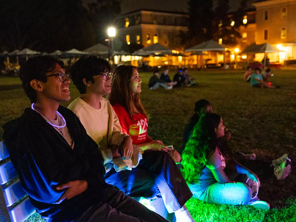 Students sit on lawn and watch a nighttime performance
