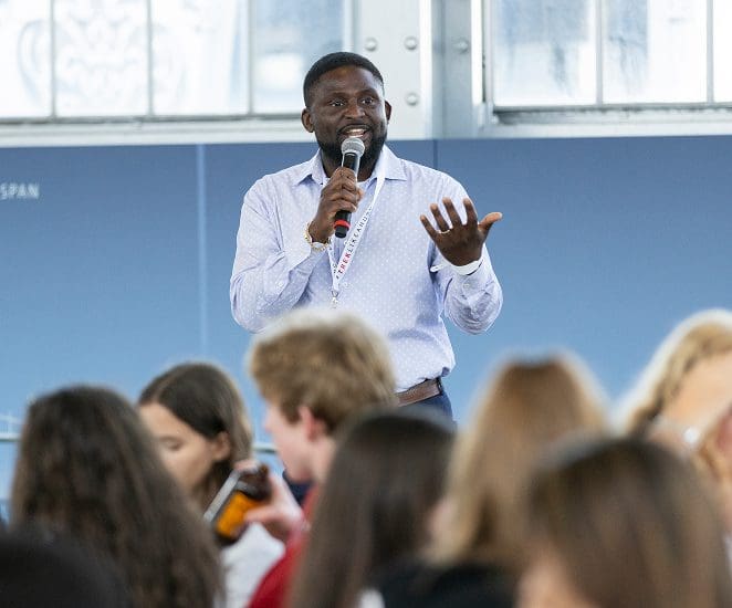 Speaker with microphone addresses groups of students seated at tables