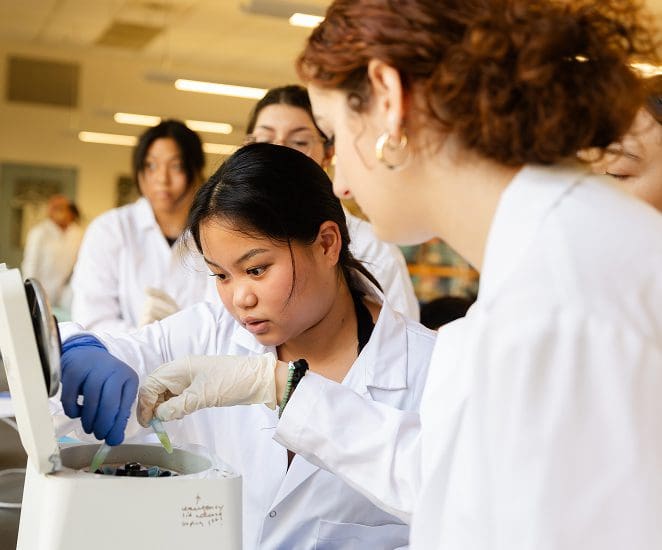 Students in lab coats place small vials of liquid into a centrifuge