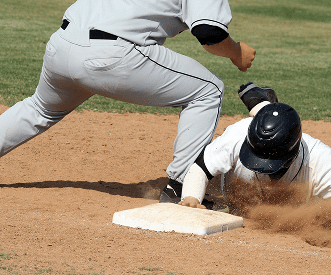 A baseball player in a white uniform slides headfirst into a base as a player in a gray uniform attempts to tag him out. Dirt is kicked up by the slide.
