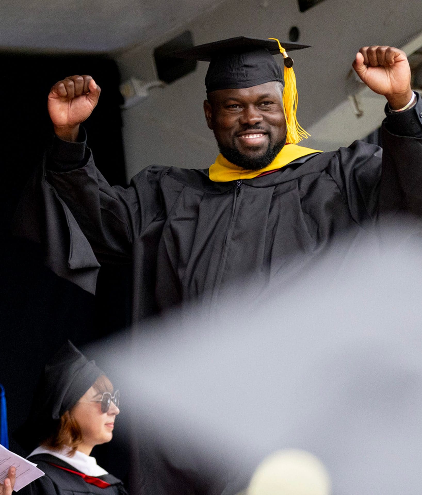 Graduating student wearing regalia celebrates with arms in the air