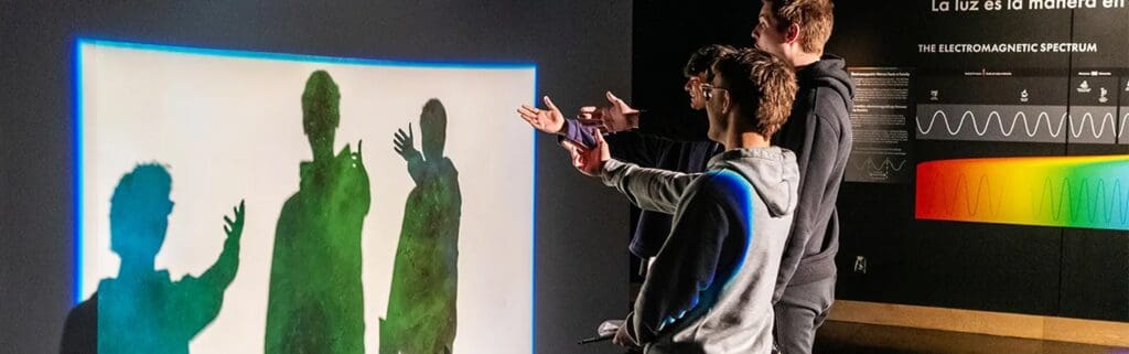 Three students interact with rainbow-hued projected shadows