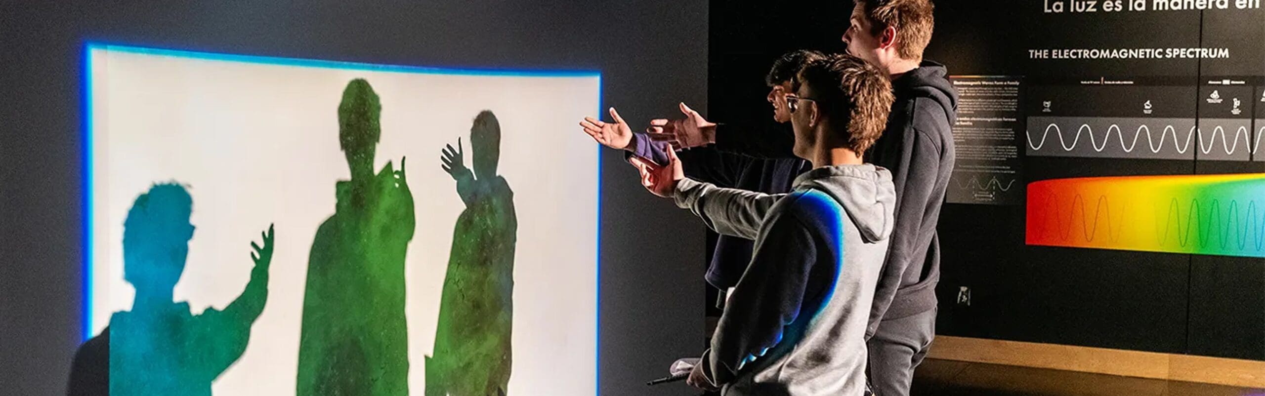 Three students interact with rainbow-hued projected shadows