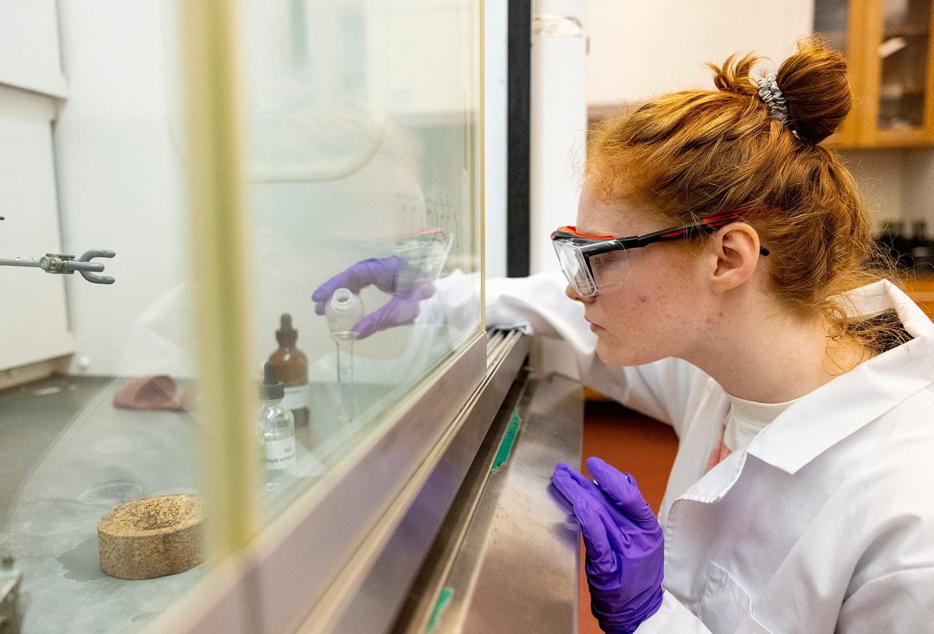 Student wearing lab coat pours liquid into test tube