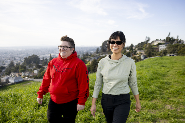 Two students walk across a green meadow in the hills above Oakland.