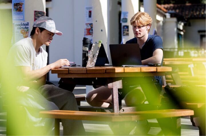 Students sit at table at Suzanne Adams Plaza on the Northeastern University Oakland campus