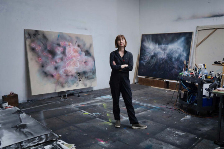Yulia Pinkusevich stands in front of two artworks from her exhibit.