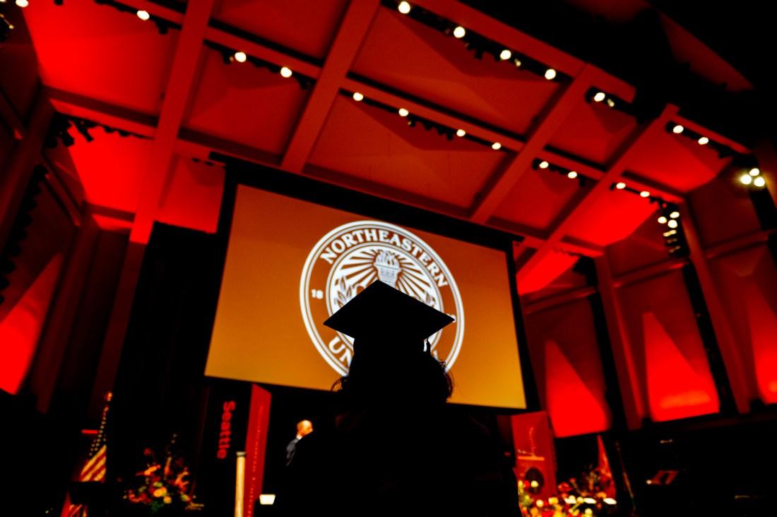 Silhouette of student wearing mortar board in a dramatically lit auditorium