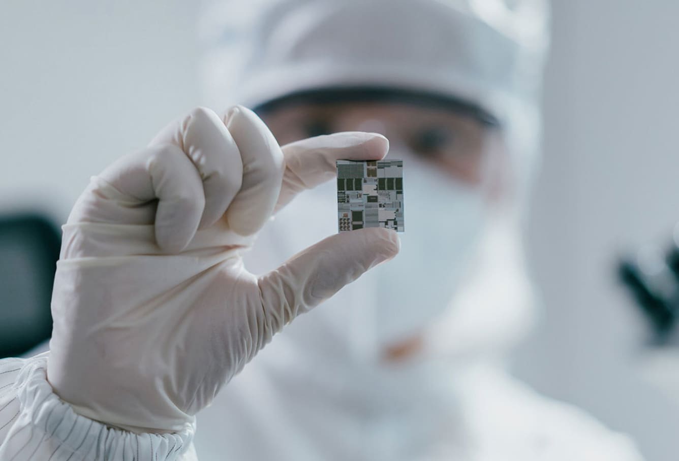 Person in clean suit holds up chip between gloved fingers